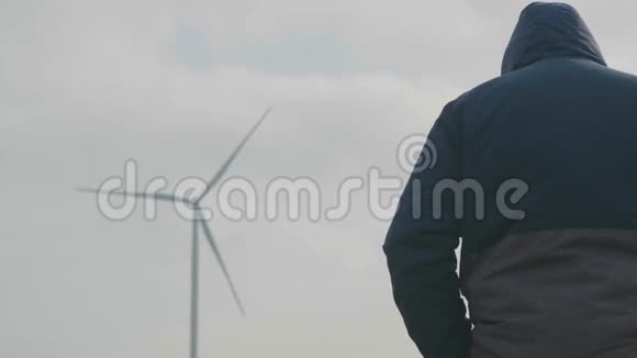 一个职业摄影师在一个多云的日子站在一个旋转的风力发电机和准备一张照片视频的预览图