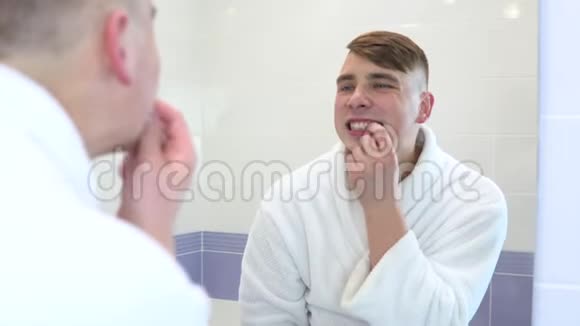 一个年轻人正在刷牙一个穿着白色外套的男人看着镜子里的牙齿开始刷牙视频的预览图