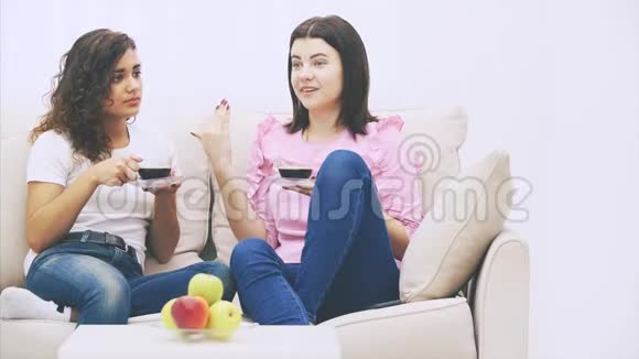 两个女朋友在温暖的家环境中坐在沙发上喝着咖啡盘子上有苹果视频的预览图