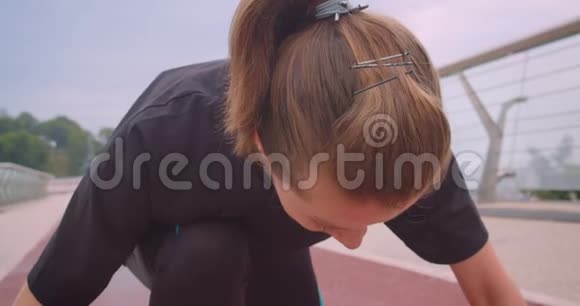 年轻的运动型女性慢跑者穿着黑色t恤坐在开始的位置上继续奔跑视频的预览图