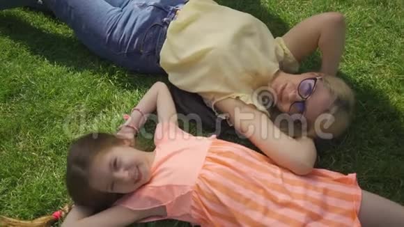 漂亮的金发母亲和她可爱的女儿躺在夏日花园或公园的草地上家庭幸福妇女与妇女视频的预览图
