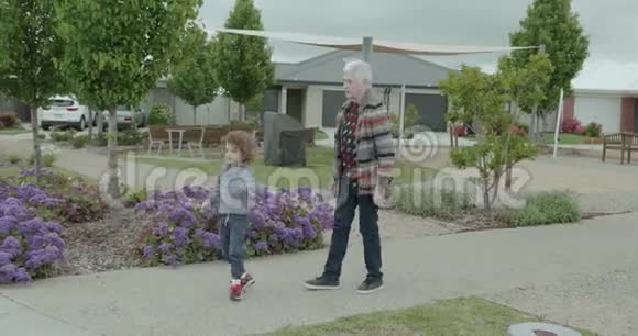 一个年长的女人和一个小男孩慢慢地走在人行道上直到他们停在路上小男孩指着什么东西视频的预览图