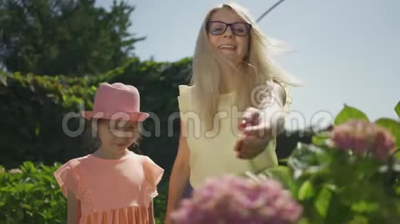 可爱的微笑母亲戴着眼镜向她的小女儿展示了公园里盛开的花朵家庭幸福妇女和女孩视频的预览图