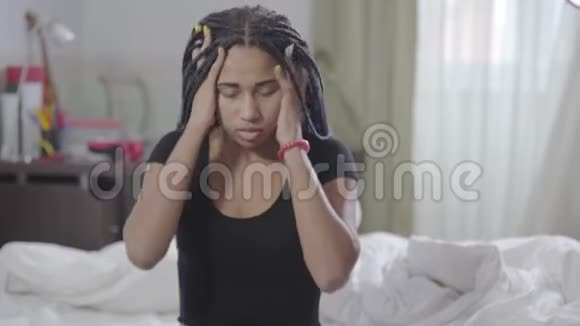 年轻的非裔美国女孩用手抱着可怕的石头揉着头落在床上的肖像累了视频的预览图