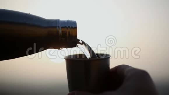 特写男性手如何将水从钢制热瓶倒入不锈钢杯背景是日落视频的预览图