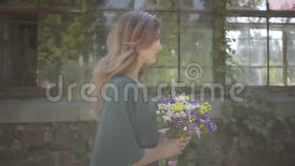 一幅美丽的年轻女子走在建筑物附近的野花的肖像夏季休息日概念视频的预览图