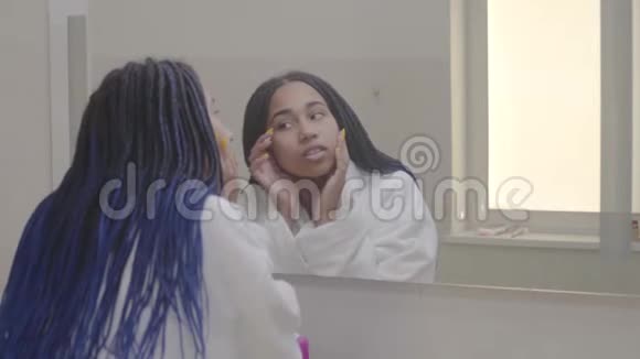 年轻漂亮的非裔美国女人在浴室里看着大镜子摸着她的脸白人少年视频的预览图