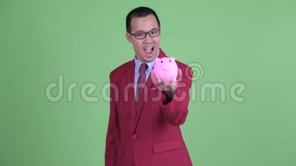 快乐的亚洲商人戴着眼镜拿着储蓄罐竖起大拇指视频的预览图