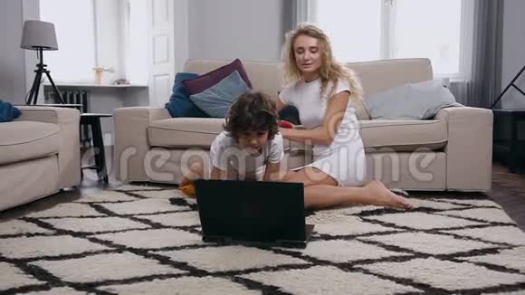 快乐无忧无虑可爱的母子坐在沙发附近的地毯上在电脑上玩电子游戏视频的预览图