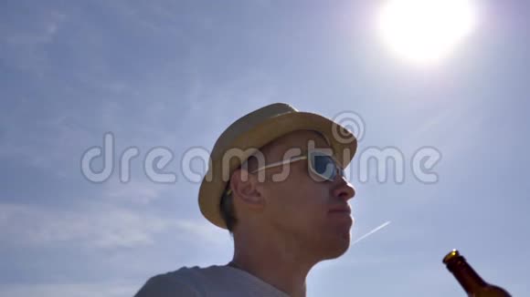 一个戴着帽子戴着眼镜的人消渴站在灿烂的阳光下视频的预览图