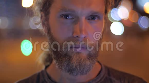 一个英俊的留着胡须的长发年轻人沉思着在傍晚的城市里直视着镜头视频的预览图