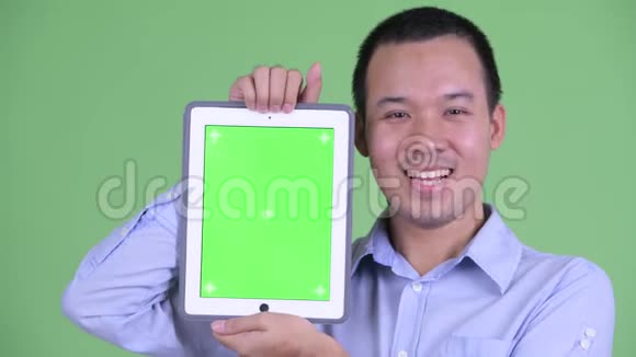 一位快乐的亚洲商人在展示数码平板电脑的同时说话视频的预览图