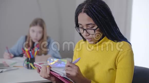 非洲裔美国学生戴眼镜看镜头微笑的肖像做家庭作业的聪明女孩视频的预览图