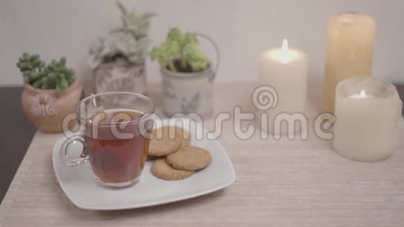 放松的概念女人手拿着一杯茶从盘子里拿出来饼干放在一张小桌子上里面有蜡烛小植物视频的预览图