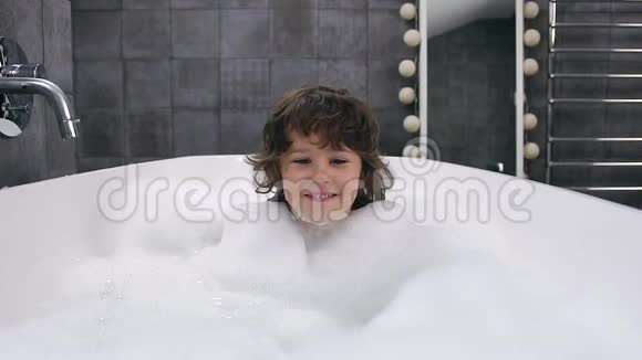 正面观看棕色头发的活泼的小男孩用泡沫洗澡看相机视频的预览图
