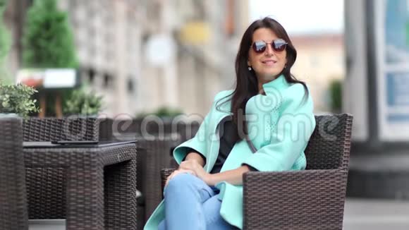 微笑迷人的女性放松坐在户外咖啡馆的椅子上享受城市背景的休息视频的预览图