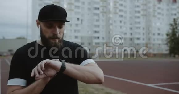 年轻有动力的男性运动员准备在跑道上跑步在智能手表上设置计时器并开始缓慢运动视频的预览图