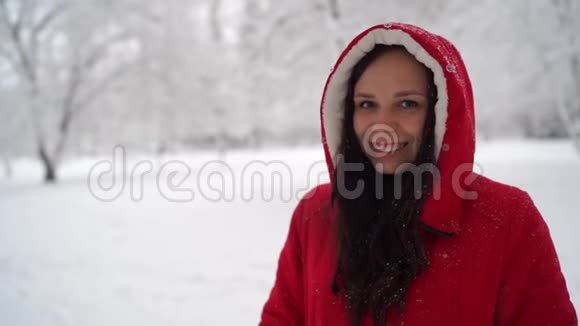 冬天穿红色夹克和引擎盖的年轻女人的肖像美丽的女士微笑着在下雪的时候高兴视频的预览图