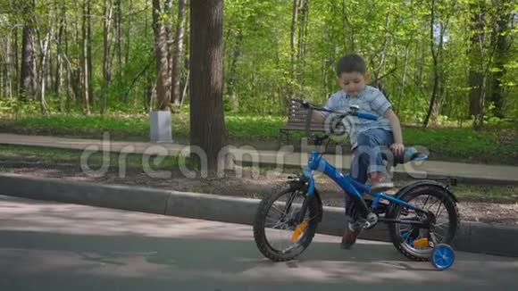 五岁的男孩在春天公园里骑一辆蓝色自行车视频的预览图