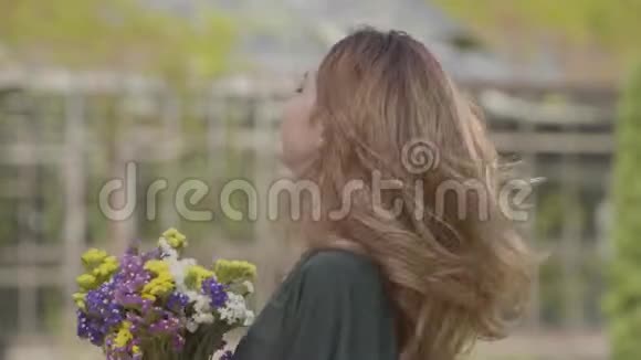 一位美丽的年轻女子的肖像她留着波浪状的头发捧着一束野花摆在户外概念视频的预览图
