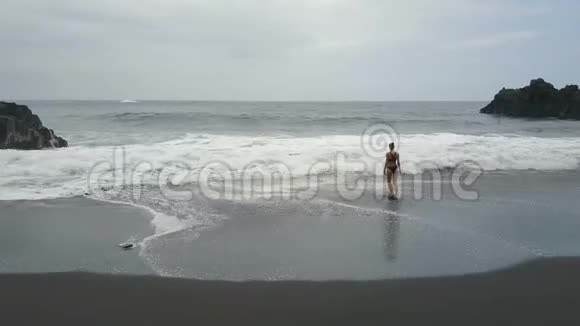在西班牙特内里费的一个黑色沙滩上一位美丽的女人走进水中举起双手视频的预览图