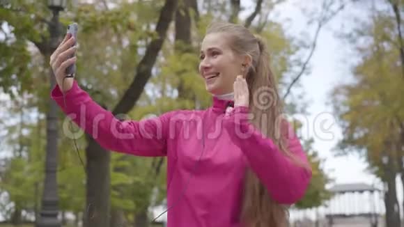 穿着粉色运动服的白种人欢快的肖像通过视频聊天竖起大拇指开始奔跑视频的预览图