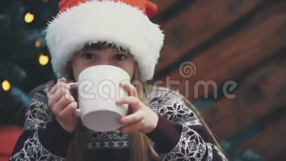 特写4k视频可爱的微笑女孩坐在家里舒适拿着一杯热巧克力在圣诞树上的木制视频的预览图