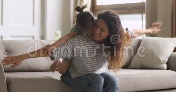 快乐妈妈背着可爱的女儿坐在沙发上视频的预览图