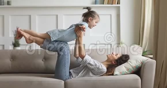 快乐妈妈举起可爱的孩子女儿在沙发上玩飞机视频的预览图