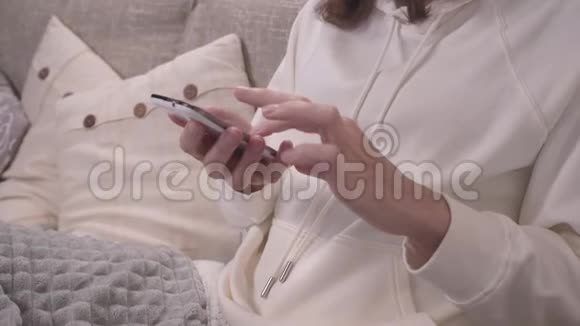 放松的概念女人坐在沙发上双腿放着一条毯子用她的智能手机从前面拿出来一边滑动视频的预览图