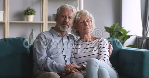 严肃快乐的老夫妇在沙发上看着摄像机视频的预览图