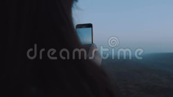 特写快乐年轻博主女士拍摄智能手机视频的神秘蓝雾日出景观慢动作视频的预览图