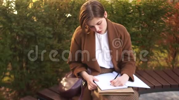 短发女孩坐在公园的长凳上在一个大笔记本上写一些东西准备考试的学生视频的预览图