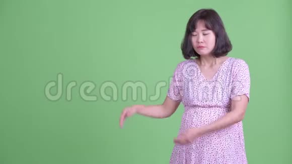 穿着衣服的亚洲孕妇向后展示并竖起大拇指视频的预览图