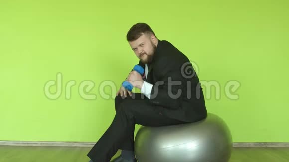 一个穿着商务服留着胡子的白种人在绿色背景下的健身房里和一个哑铃订婚复制空间视频的预览图