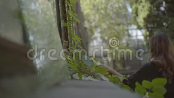 年轻女子在花园里散步时看着老房子的窗户的肖像夏季概念视频的预览图