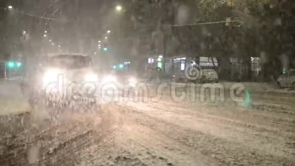 汽车在冬季暴风雨和暴风雪中行驶城市里夜里下着大雪大雪阻碍了城里的道路交通夜晚视频的预览图