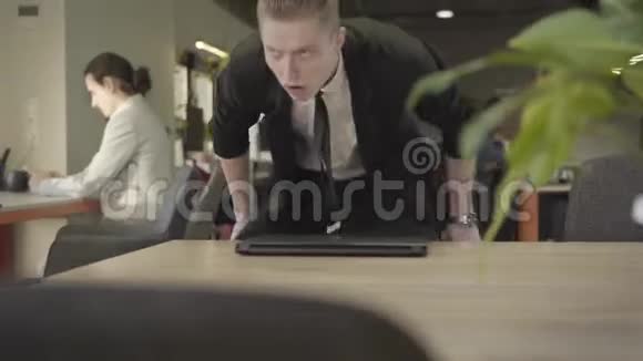 严肃的男性白种人办公室工作人员坐在桌子旁打开笔记本电脑穿正式西装的红头发男子的肖像视频的预览图