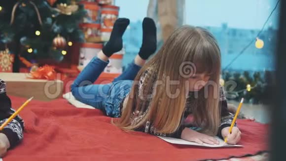 可爱的小男孩穿着节日礼服躺在她的腹部写信给圣诞老人圣诞树上有灯和礼物视频的预览图