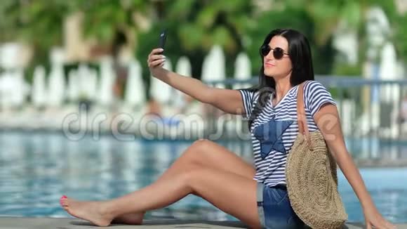 微笑旅游妇女自拍使用智能手机游泳池棕榈背景视频的预览图