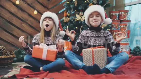 有趣的4k视频小兄弟姐妹在圣诞帽练习瑜伽在家里的红地毯在圣诞节时间视频的预览图
