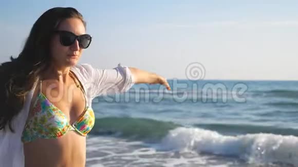 美丽的黑发美女戴着太阳镜沿着海洋海岸奔跑享受自由有魅力的女人在玩的画像视频的预览图