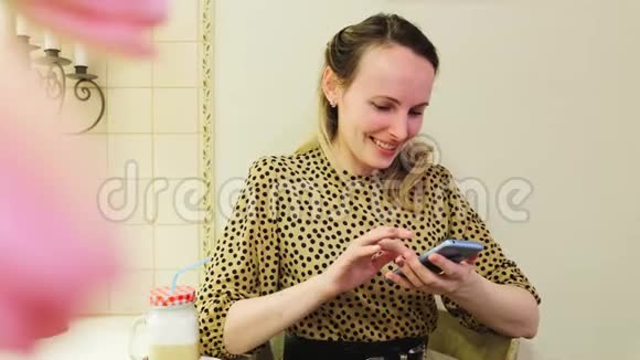 一个穿着裙子的年轻迷人的女孩坐在咖啡馆里使用智能手机肖像视频的预览图