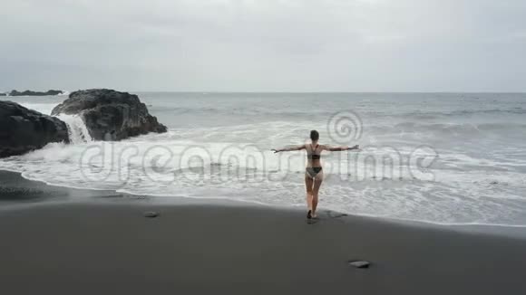 在西班牙特内里费的一个黑色沙滩上看到一个女人在水中奔跑海浪冲破形成白色视频的预览图