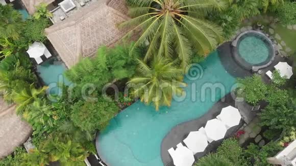 空中无人机飞行从上往下看豪华酒店有草屋顶别墅和热带丛林和棕榈树的游泳池视频的预览图