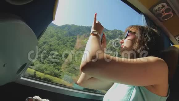 带智能手机的旅游女孩通过公共汽车窗口拍摄自然景观观光旅行和旅游视频的预览图