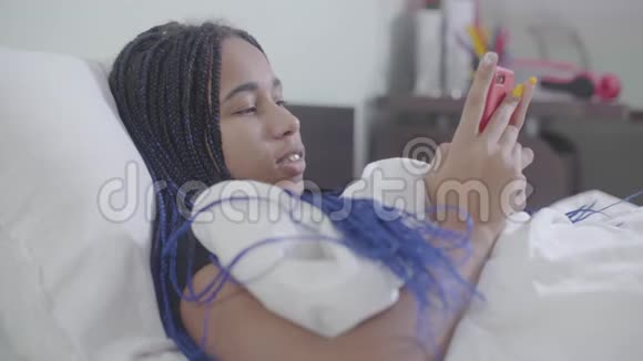 非裔美国女孩戴着可怕的使用智能手机把它收起来沉思地抬头看青少年使用视频的预览图