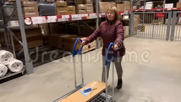 穿夹克的女人在一家自助家具店里拿着一辆大型购物手推车这是一种购物概念视频的预览图
