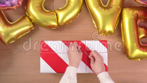 一位穿着白色毛衣的年轻女士正在包装用金色气球包装漂亮的礼品盒准备节日准备视频的预览图