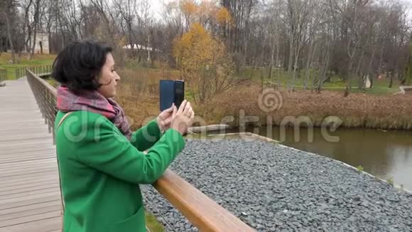 秋天阴天女人在公园里拍池塘的照片从后面看视频的预览图